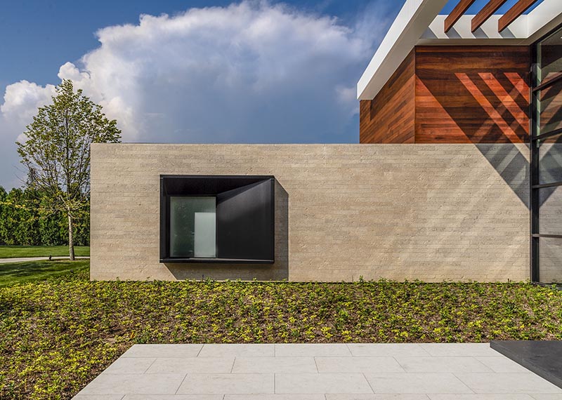 The oversized black steel-clad window frame intentionally juts from the stone entry wall of this modern house, and with its design, it casts a variety of shadows throughout the day, depending on the sunlight or the light coming from within the house. #ProtrudingWindow #WindowDesign #ModernArchitecture #ModernHouse