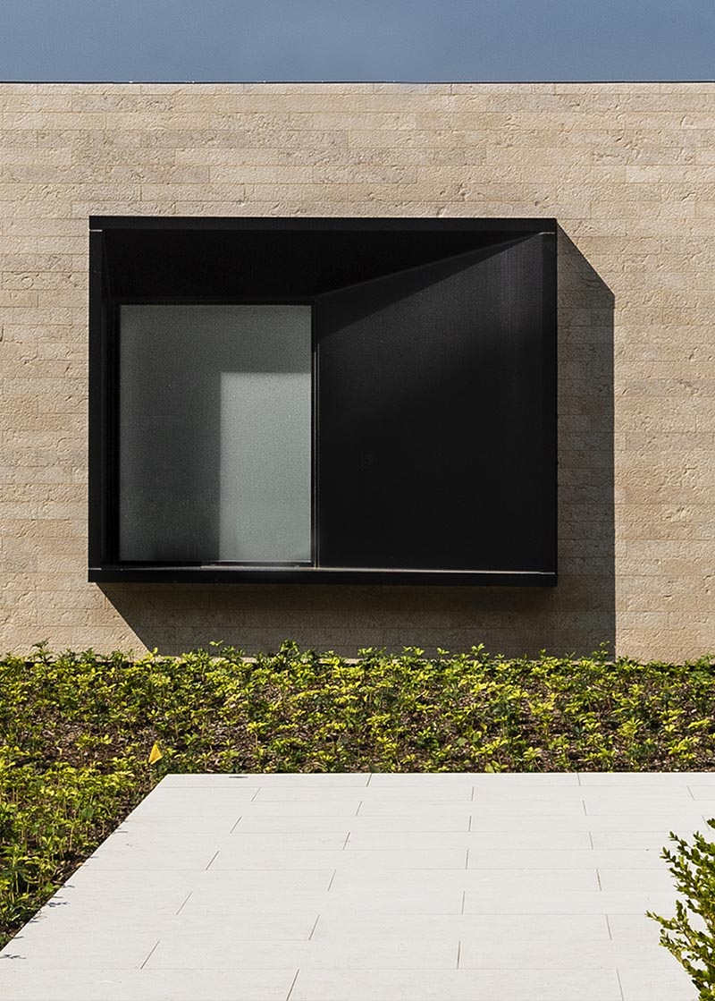 The oversized black steel-clad window frame intentionally juts from the stone entry wall of this modern house, and with its design, it casts a variety of shadows throughout the day, depending on the sunlight or the light coming from within the house. #ProtrudingWindow #WindowDesign #ModernArchitecture #ModernHouse