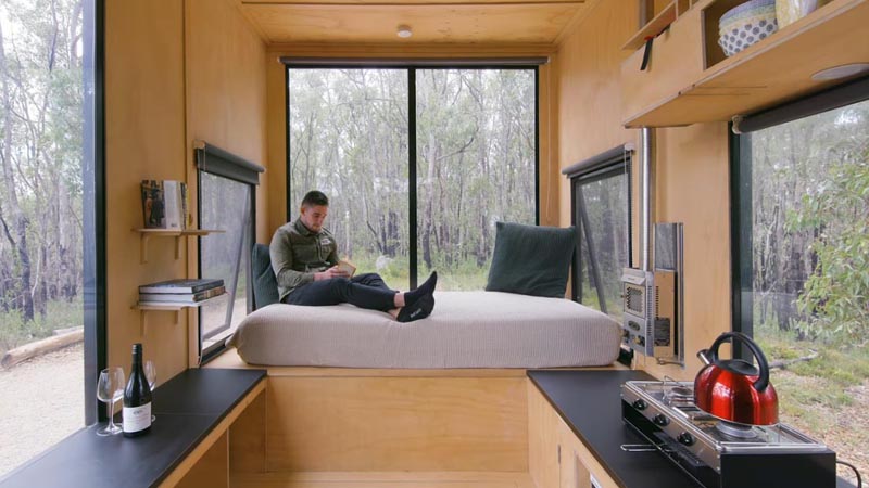 At one end of this modern tiny house is a day bed that's been elevated to create a sense of separation from the breakfast bar and kitchen. #DayBed #TinyHouse #TinyHome