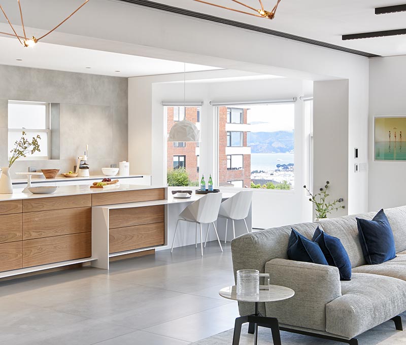 This modern kitchen has plenty of windows, minimalist cabinets, and white countertops with matching white furniture to ensure that the space is bright and welcoming. #ModernKitchen #KitchenDesign #KitchenIdeas #BrightKitchen