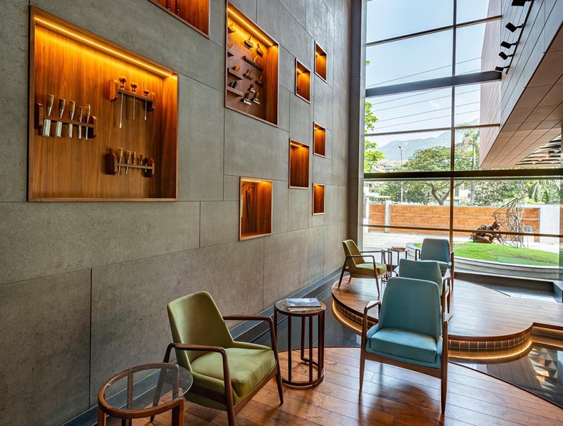 This large and open lobby features a wall with wood-lined built-in shelving, that uses hidden lighting to highlight the woodworking tools on display. #WoodLinedShelves #BuiltInShelving #ShelvingIdea #ShelfLighting #HiddenLighting