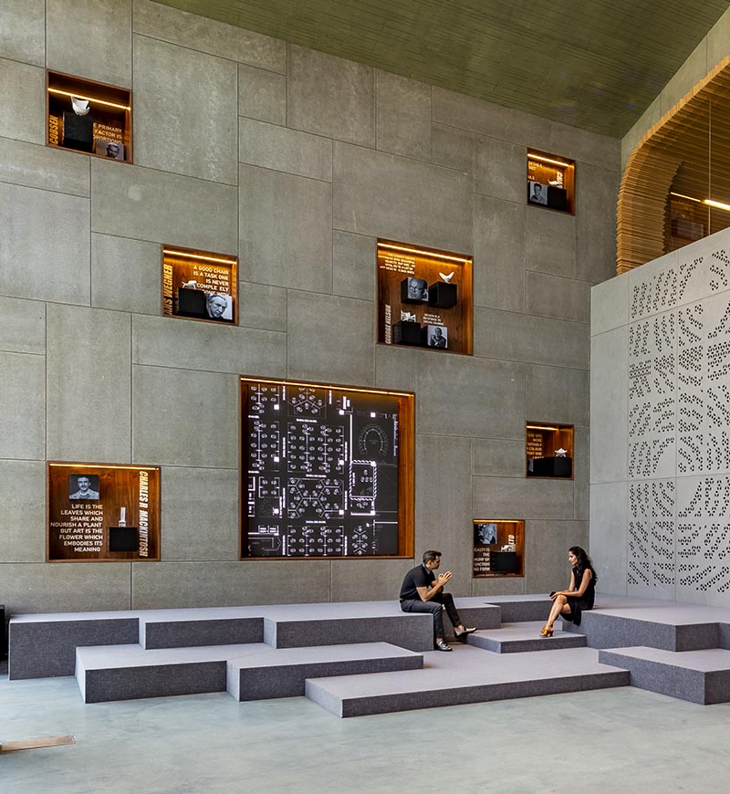 This large and open lobby features a wall with wood-lined built-in shelving, that uses hidden lighting to highlight the woodworking tools on display. #WoodLinedShelves #BuiltInShelving #ShelvingIdea #ShelfLighting #HiddenLighting