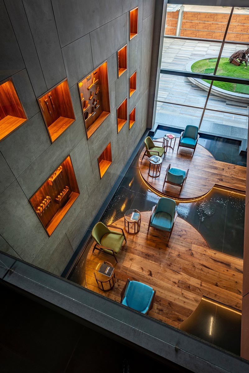 This large and open lobby features a wall with wood-lined built-in shelving, that uses hidden lighting to highlight the woodworking tools on display. #WoodLinedShelves #BuiltInShelving #ShelvingIdea #ShelfLighting #HiddenLighting