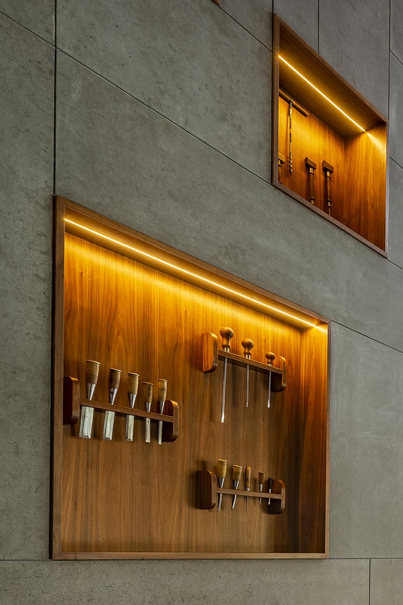 This large and open lobby features a wall with wood-lined built-in shelving, that uses hidden lighting to highlight the woodworking tools on display. #WoodLinedShelves #BuiltInShelving #ShelvingIdea #ShelfLighting #HiddenLighting