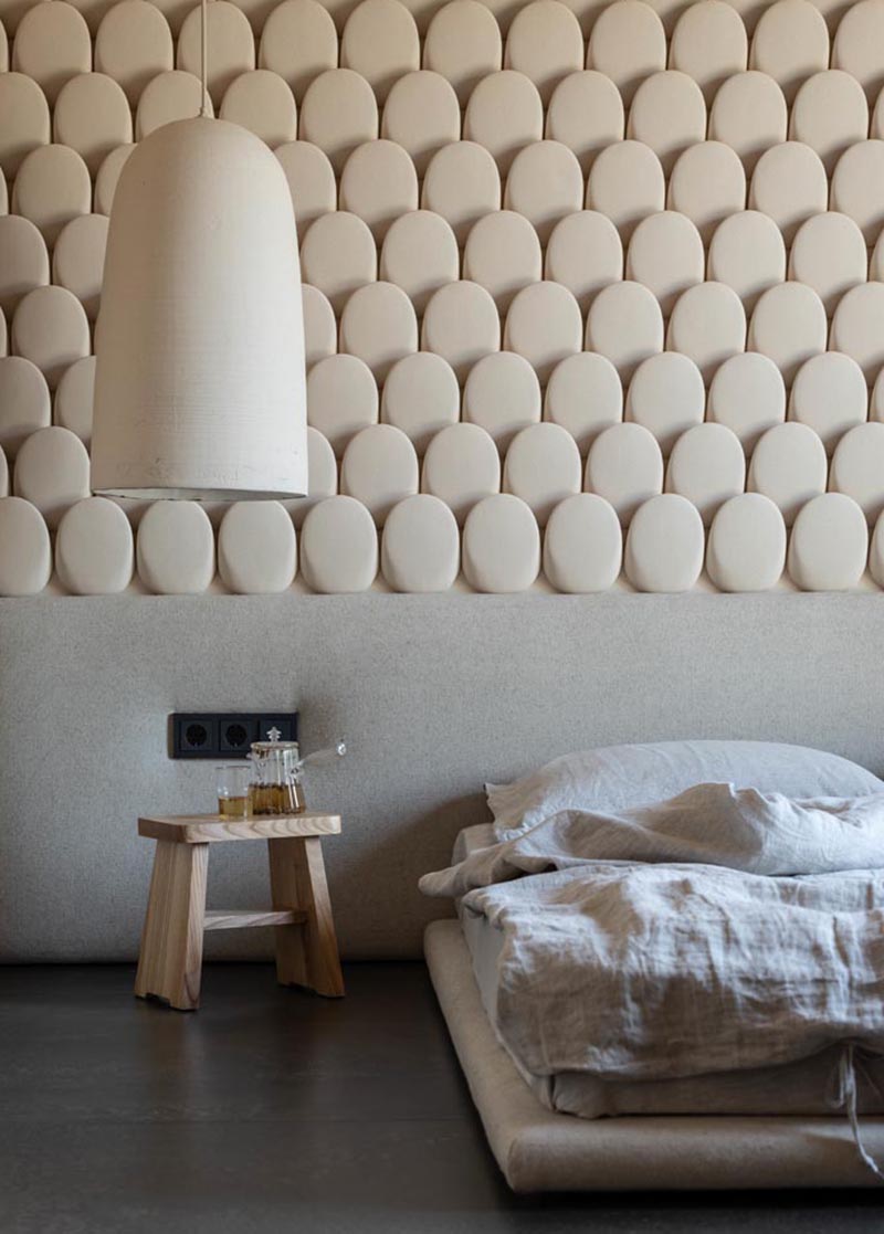 This modern bedroom features an eye-catching accent wall, that looks like small rounded stones, and helps to add texture to the room. #AccentWall #ModernBedroom #SculpturalWall #BedroomDesign