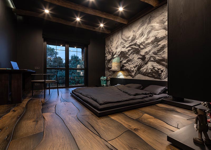 This modern and dramatic bedroom, inspired by the Japanese philosophy of wabi-sabi that finds beauty and harmony in imperfections, features a low tatami-style bed, that's positioned on the dark wood floor that looks like puzzle pieces that fit together. #ModernBedroom #WoodFloors #InteriorDesign #BedroomDesign #WallMural