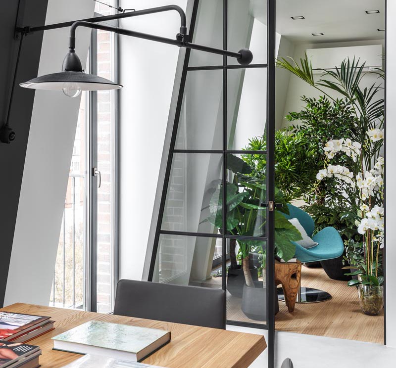 This modern apartment features an indoor plant room that can be seen through a black-framed glass wall, with a door that opens to reveal a quiet and peaceful sitting area. #IndoorGarden #IndoorPlantRoom #IndoorGardenRoom #ReadingNook #InteriorDesign