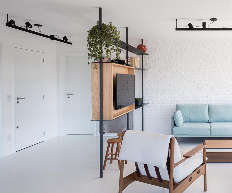 This modern open plan interior features a room divider that separates the entryway from the living room. It also provides shelving and a designated place for a mounted television. #RoomDivider #ModernRoomDivider #InteriorDesign #LivingRoom