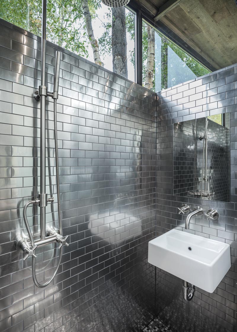 This tiny house has a full-size bathroom with stainless steel subway tiles that cover the walls, and windows that meet the roof. #Bathroom #TinyHouseBathroom #TinyHouse #StainlessSteelTiles