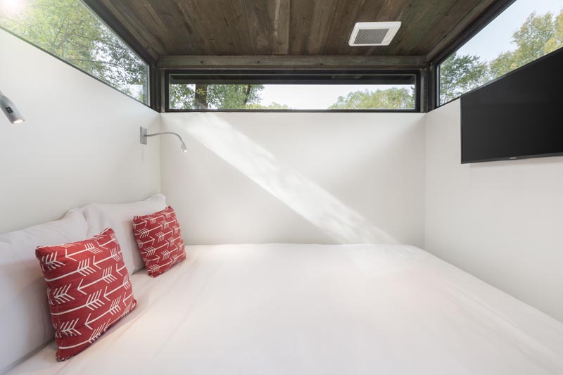 Long narrow windows wrap around the bedroom in this tiny house, while a pair of sconces provide light at night. #TinyHouse #TinyHome #Bedroom