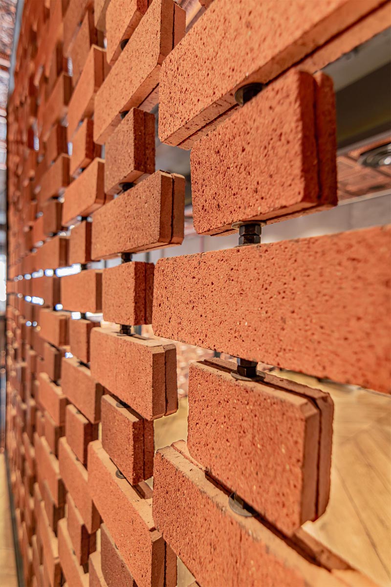 Open brick walls wrap around the different areas of this restaurant, like above the kitchen and along the stairs. They provide visiual interest and a sense of privacy on the upper level of the interior, without blocking the light. #RestaurantDesign #BrickWalls #ScreenIdea #BrickScreen