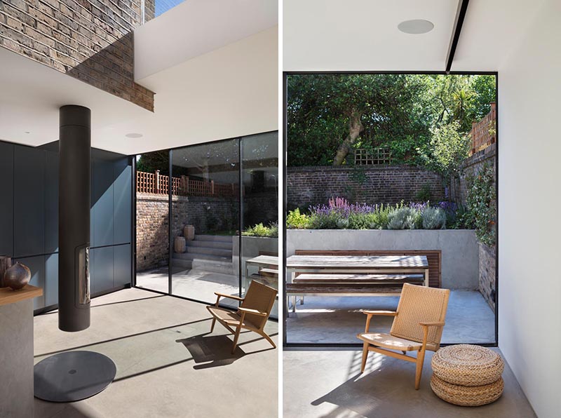 This modern glass house extension features a pivoting fireplace, while floor-to-ceiling sliding doors provide access to the patio and raised secluded garden. #PivotingFireplace #FireplaceIdeas #Patio #Garden #SlidingDoors