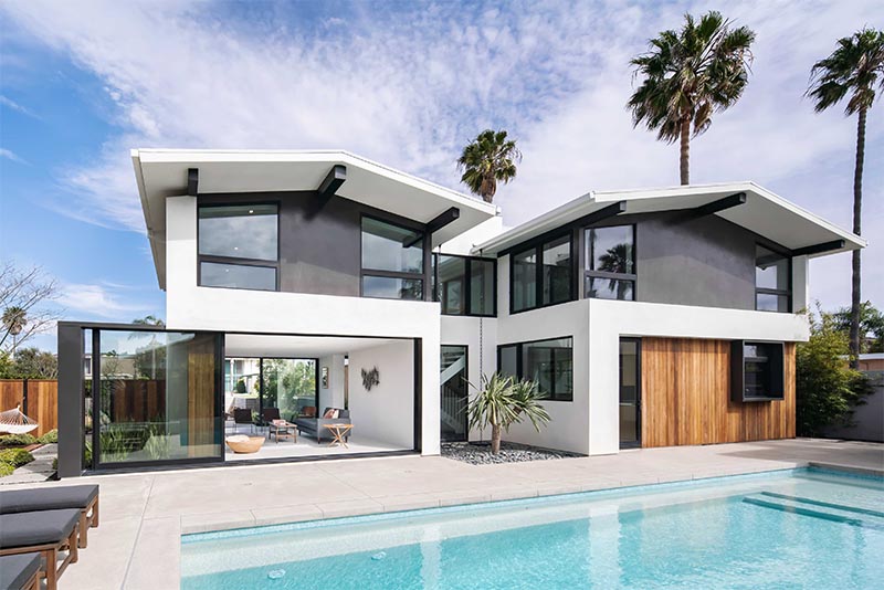 A full-height wall-to-wall glass door with a black frame, opens up the living room of this modern house and connects it to the patio that surrounds the pool. #GlassWall #Architecture #SlidingWall #ModernHouse