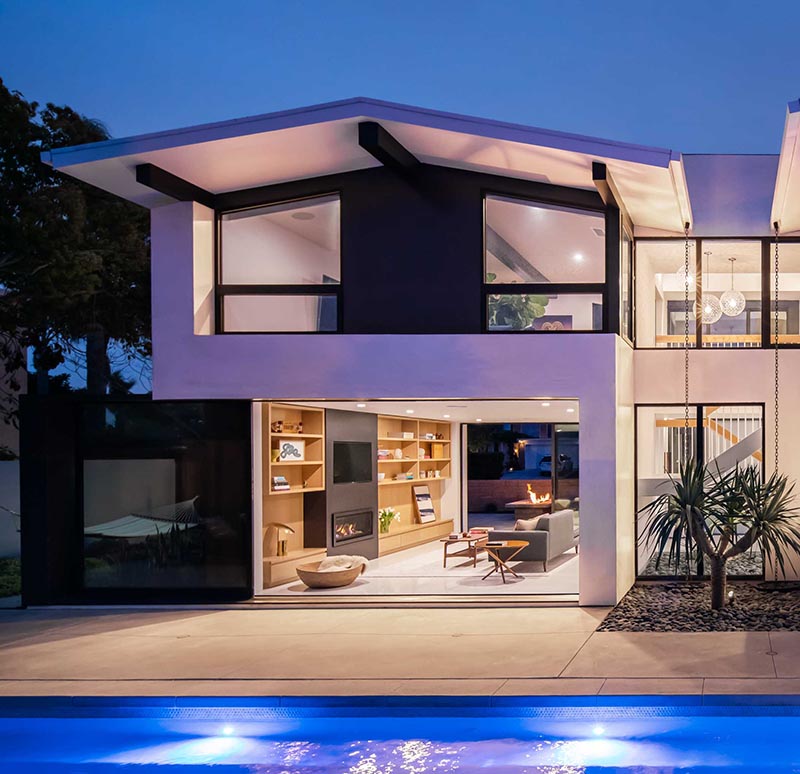 A full-height wall-to-wall glass door with a black frame, opens up the living room of this modern house and connects it to the patio that surrounds the pool. #GlassWall #Architecture #SlidingWall #ModernHouse