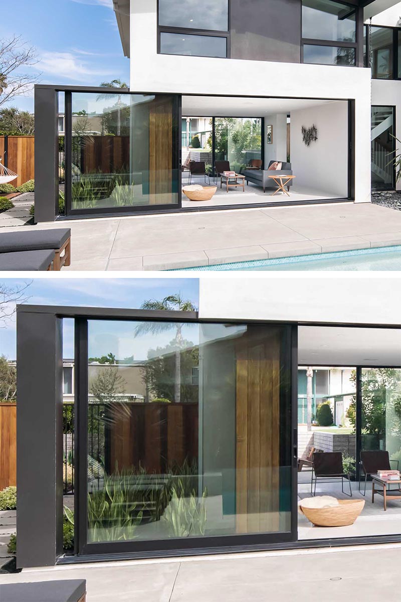 A full-height wall-to-wall glass door with a black frame, opens up the living room of this modern house and connects it to the patio that surrounds the pool. #GlassWall #Architecture #SlidingWall #ModernHouse