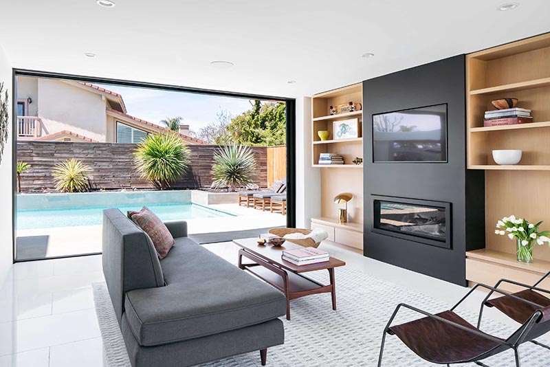 A full-height wall-to-wall glass door with a black frame, opens up the living room of this modern house and connects it to the patio that surrounds the pool. #GlassWall #Architecture #SlidingWall #ModernHouse