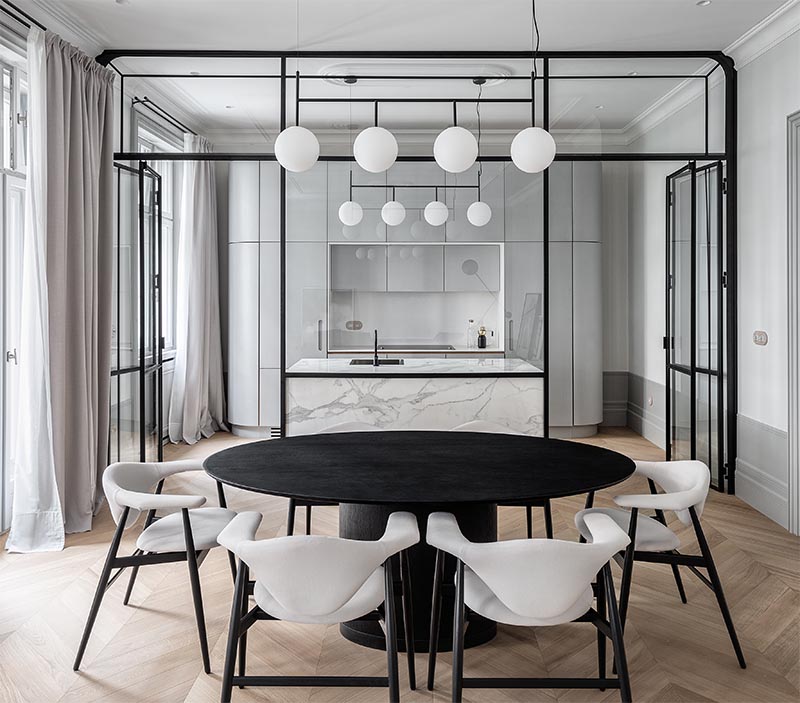 This updated apartment features an eye-catching, black steel framed glass wall that separates the kitchen from the dining room. There's also a grey marble island that complements the grey kitchen cabinets. #ModernKitchen #GlassWall #InteriorDesign #Interiors #GlassPartition