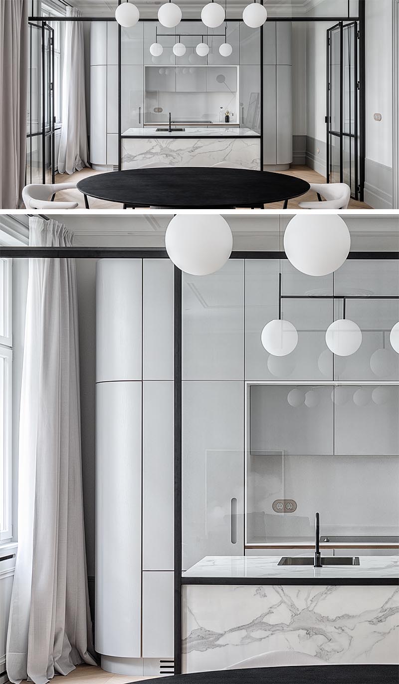 This updated apartment features an eye-catching, black steel framed glass wall that separates the kitchen from the dining room. There's also a grey marble island that complements the grey kitchen cabinets. #ModernKitchen #GlassWall #InteriorDesign #Interiors #GlassPartition