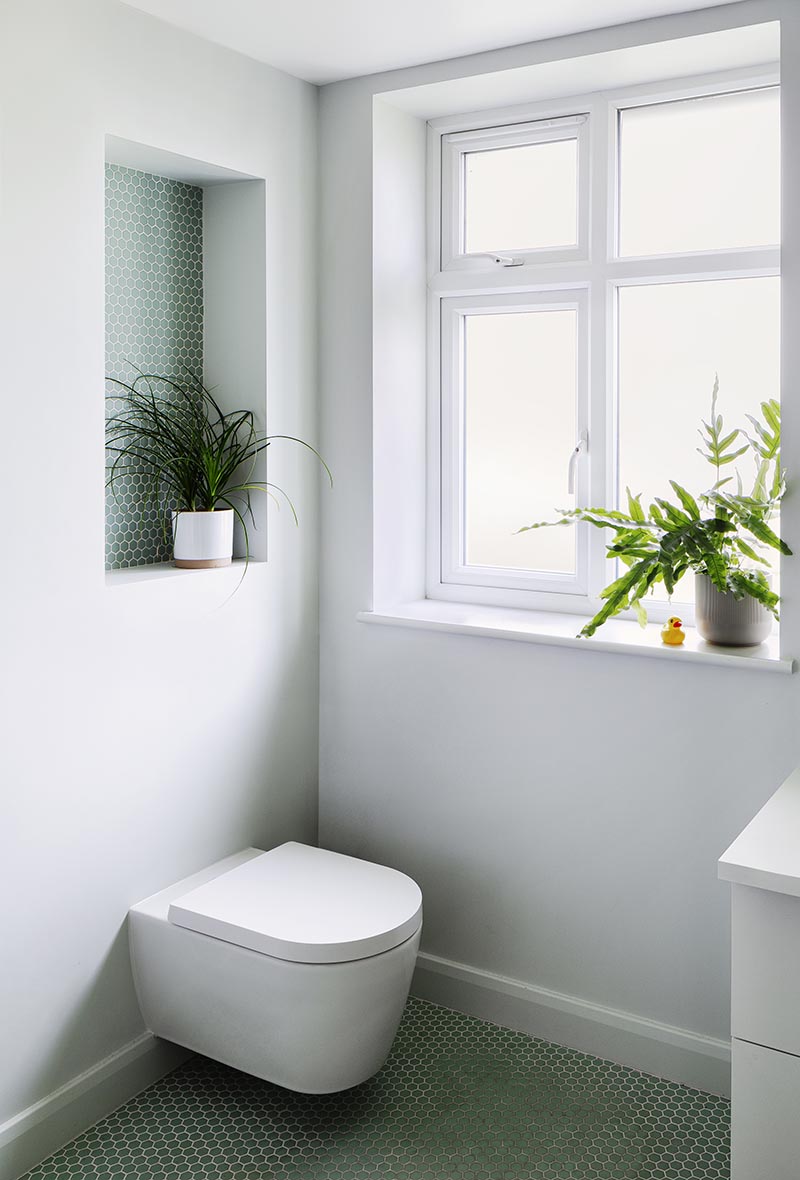 This modern bathroom features a recessed shelf, which is large enough to display a plant, and includes small hexagon penny tiles with white grout. It also helps to add a pop of color to the plain grey wall, and draws attention away from the toilet below. #BathroomShelf #BathroomIdeas #RecessedShelf #PennyTile #BathroomDesign