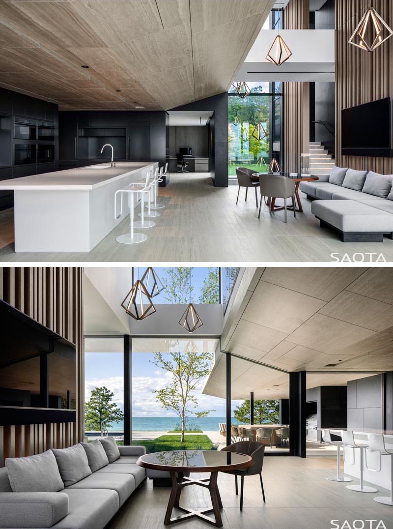 A tall partition separates the dining area from a secondary seating area that faces the modern black kitchen with a large white island. #ModernKitchen #BlackAndWhiteKitchen #MinimalistKitchen