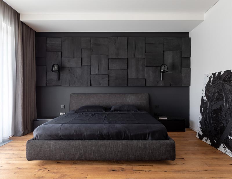 In this modern black bedroom, there's a black wall that provides a backdrop for the matching bed, while a blackened wood panel accent wall adds interest and texture to the room. #BlackBedroom #BlackAccentWall #BlackWoodAccentWall #WoodAccentWall #ModernBedroom