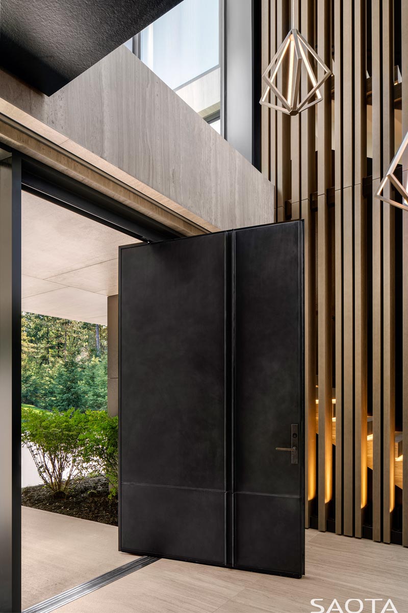 Welcoming visitors to this modern lake house is an oversized steel pivoting front door. #SteelFrontDoor #PivotingFrontDoor #OversizedFrontDoor