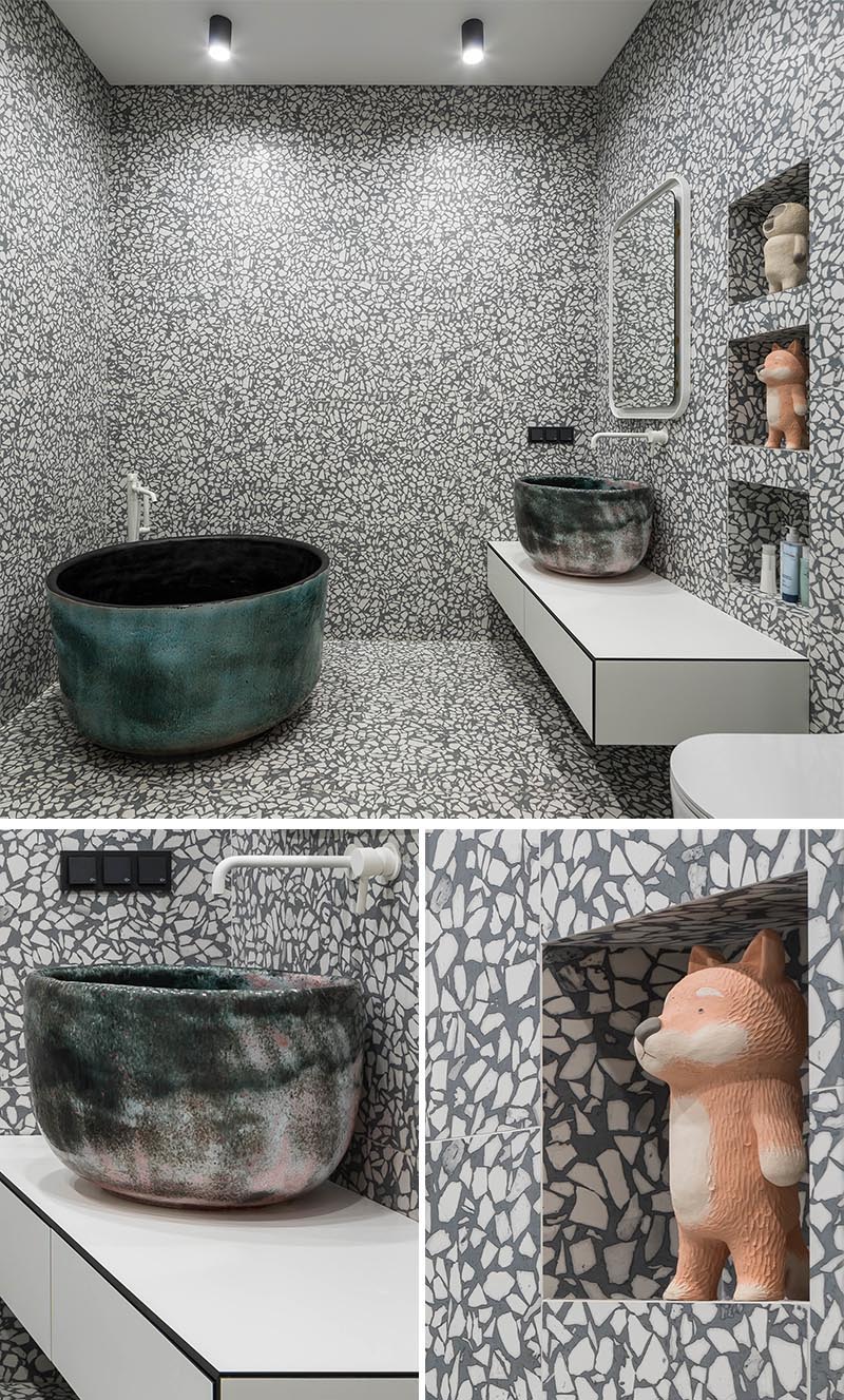 A grey and white aggregate large format tile has been installed in this modern bathroom, and covers the walls and floor, creating an almost art-like experience when using the bathroom. #GreyAndWhiteBathroom #GreyBathroom #BathroomIdeas #SoakingTub #ShelvingNiche #ModernBathroom #FloatingVanity