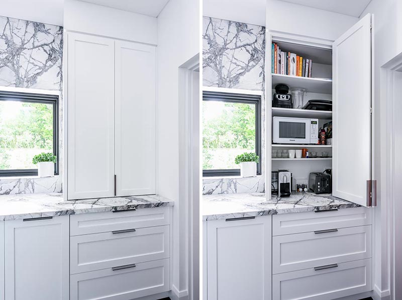 To keep these modern kitchen counters clear of clutter, a cabinet with a folding door has been dedicated to storing the microwave, cook books, toaster, and coffee machine. #KitchenDesign #KitchenIdeas #KitchenStorage #KitchenOrganization