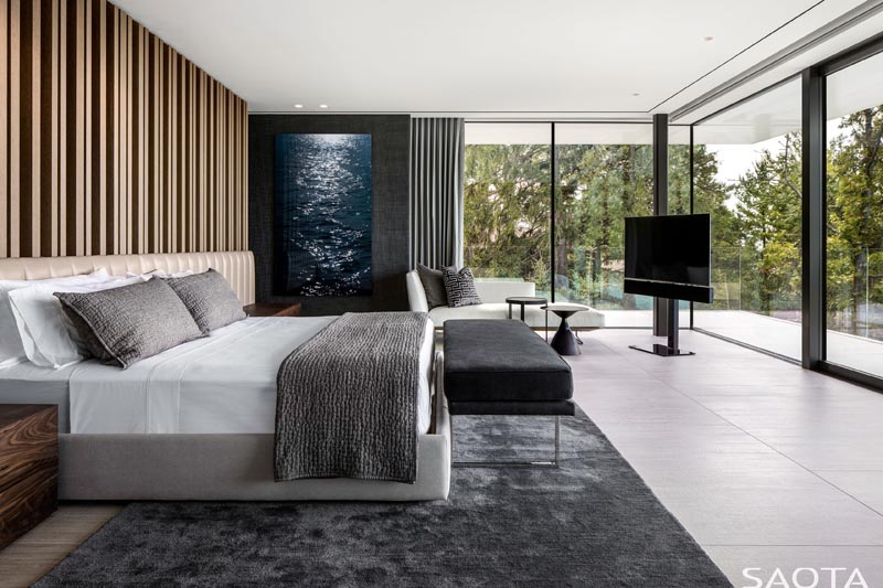 In this modern master bedroom, walls of glass provide plenty of natural light, and when privacy is needed, grey curtains that match the contemporary rug can be drawn. #MasterBedroom #GlassWalls #GreyCurtains