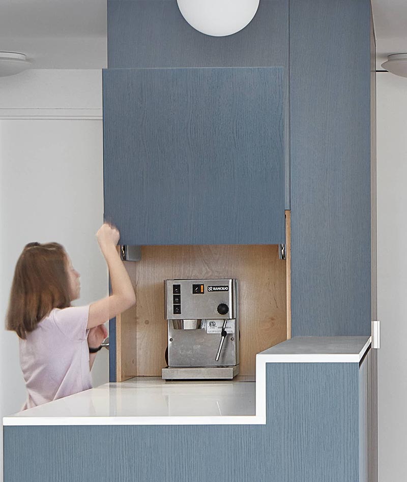 Aiming to keep the countertops clutter free, this appliance garage blends into the surrounding matte blue cabinets of this modern kitchen. #ApplianceGarage #CoffeeStation #KitchenDesign #MatteBlueKitchen #WhiteCountertops