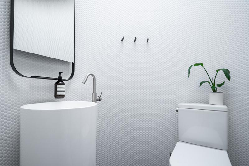 This modern circular bathroom has walls of white penny tiles, a curved pedestal vanity with a rounded edge mirror, and a toilet. #Bathroom #RoundBathroom #PennyTiles #PedestalVanity