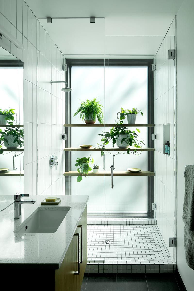 In this modern bathroom, wood shelves against a frosted window provide a place to display plants in the shower. #ModernBathroom #ShowerShelves #ShowerWithPlants #Plants #Shelving #BathroomIdeas