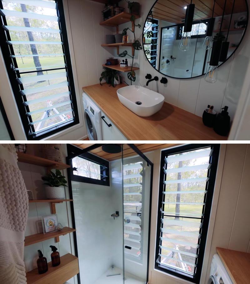 In this modern tiny house bathroom, there's a large vanity with that sits below a round mirror. There's also a full-size shower, a toilet, and a washing machine. #TinyHouseBathroom #SmallBathroom