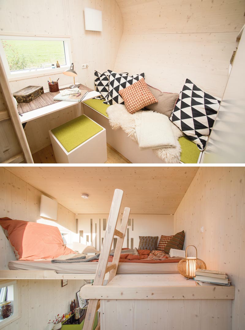 At the end of this modern tiny house is a living room that features a built-in bench with scattered pillows, and a small small desk that's positioned to take in the views from the window. A ladder leads next to the desk leads up to the sleeping loft, that's located above the bathroom. #TinyHouse #ModernTinyHouse #TinyHome #TinyHomeBedroom #LoftedBedroom
