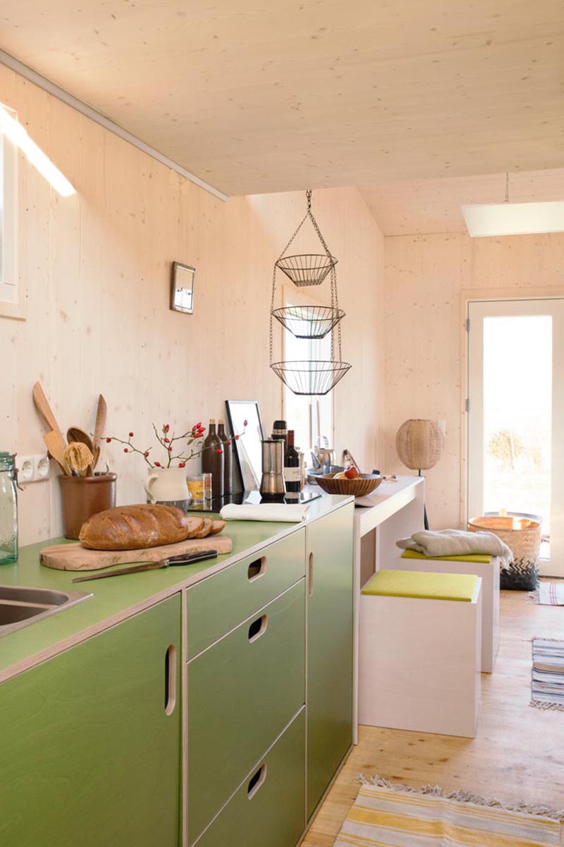 This modern tiny house has a kitchen that features minimalist green cabinets with cut-out handles. #TinyHouseKitchen #TinyHouseDesign #TinyHomeKitchen #SmallKitchen