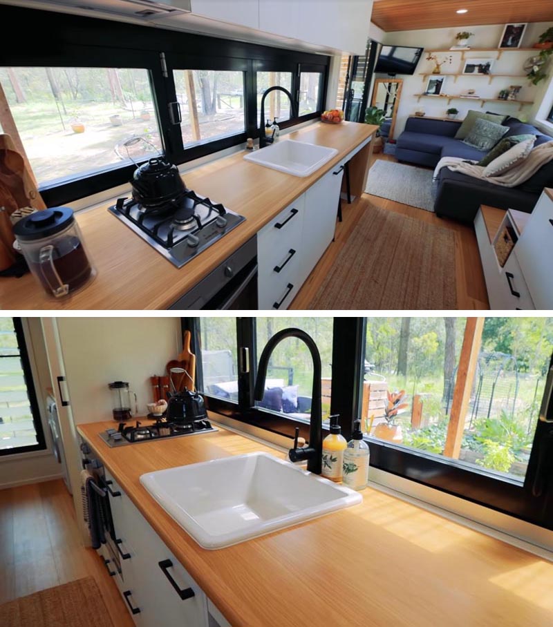 In this modern tiny house kitchen, light wood countertops and white cabinets help to keep the interior bright, while the black framed windows open up to provide direct access to the bar outside. #TinyHouseKitchen #SmallKitchen #TinyHouseIdeas