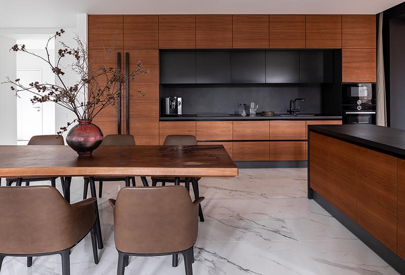 This modern warm wood kitchen and dining area includes a palette of shades ranging from cinnamon to chestnut, as well as darker elements, like the hardware and kitchen backsplash. #WarmWoodKitchen #WoodKitchen #KitchenDesign #WoodDiningTable