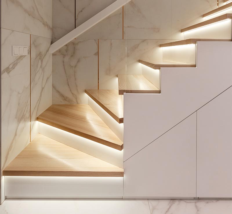 These modern wood stairs have a tread with an overhang (or nosing) that extends past the riser, allowing room for a thin strip of lighting to be attached to the underneath surface. #Stairs #StairsWithLighting #StairDesign #HiddenLighting