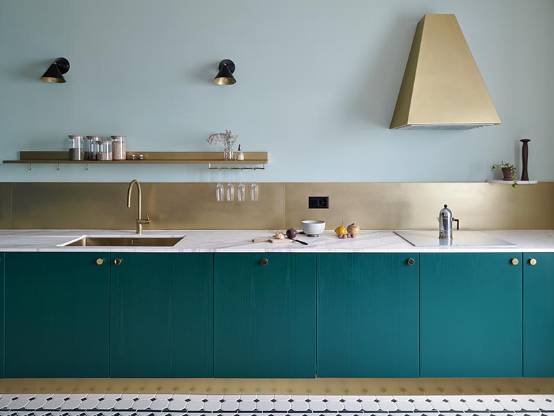 Sitting against a backdrop of mint green walls, the bronze backsplash and range hood in this modern kitchen add a luxurious metallic touch that stands out against the teal cabinets. #KitchenIdeas #BronzeKitchenAccents #TealCabinets #BronzeRangeHood