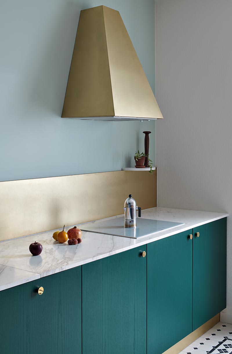Sitting against a backdrop of mint green walls, the bronze backsplash and range hood in this modern kitchen add a luxurious metallic touch that stands out against the teal cabinets. #KitchenIdeas #BronzeKitchenAccents #TealCabinets #BronzeRangeHood