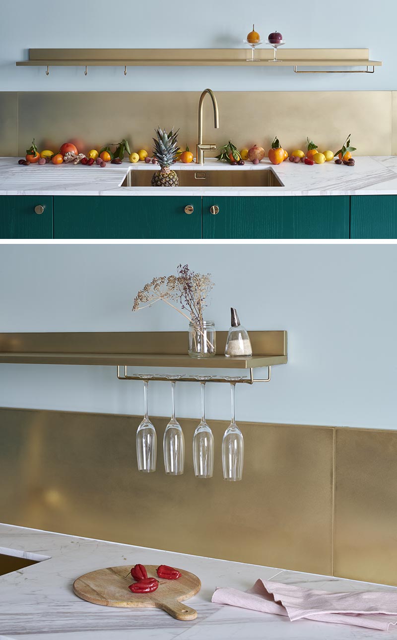 This modern kitchen has a bronze backsplash runs the length of the kitchen, and is complemented by the inclusion of a floating shelf, an undermount sink, and matching faucet. #KitchenDesign #KitchenIdeas #BronzeBacksplash #ModernKitchen