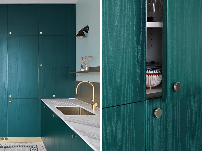 At the end of this modern kitchen, there's a wall of teal-stained wood cabinets that have small round bronze handles. Black scones provide additional light to the kitchen and tie in with the black tile featured on the floor. #TealCabinets #TealKitchen #KitchenIdeas #BronzeHardware