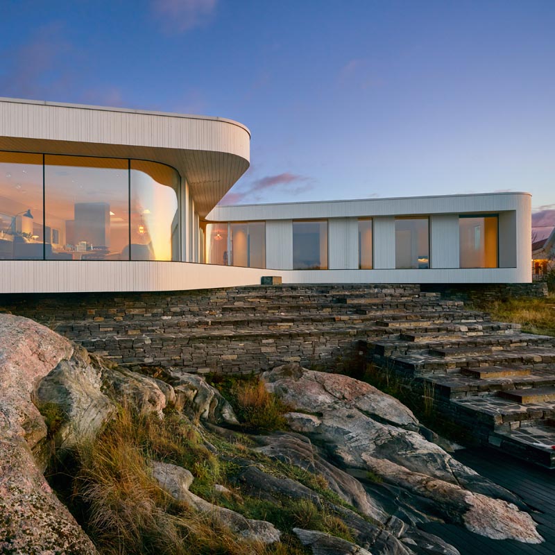 A modern villa with curved glass windows, that sits on a stone base.