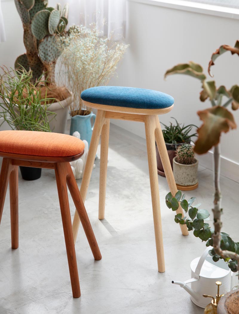 A modern wood kitchen stool with an upholstered cushion.