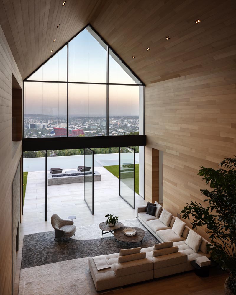 Using materials like wood, concrete, and stone, the designers of this modern barn-inspired house were able to create a warm and natural interior for the home, while travertine floors extend from inside to outside. #GreatRoom #Architecture #GabledCeiling #PivotingDoors