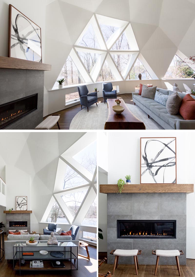 The newly updated interior of this geodesic dome house features bright white walls and modern furnishings feature throughout, like in the living room. The fireplace, which sits next to a large section of windows, has a limestone surround topped with a custom oak mantel that complements the hardwood flooring. #GeodesicDome #LivingRoom #Fireplace #TriangleWindows
