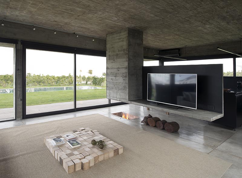 Designed as a sculptural element that separates the dining room and the living room, this modern hanging concrete divider has a chimney built into it on one end, and the other is a platform for holding the television. Underneath, the fireplace has been built into the ground. #Fireplace #RoomDivider #ConcreteDivider #HangingConcreteChimney