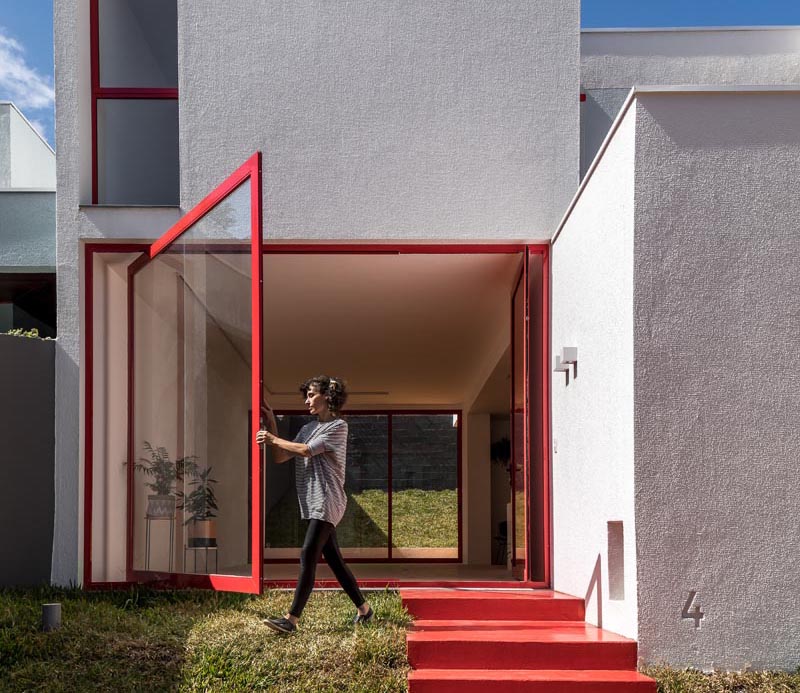 Nommo Arquitetos has recently completed the design of a house in Curitiba, Brazil, that showcases a large pivoting window next to the front door. #PivotingWindow #LargePivotWindow #RedFrontDoor #RedWindowFrames
