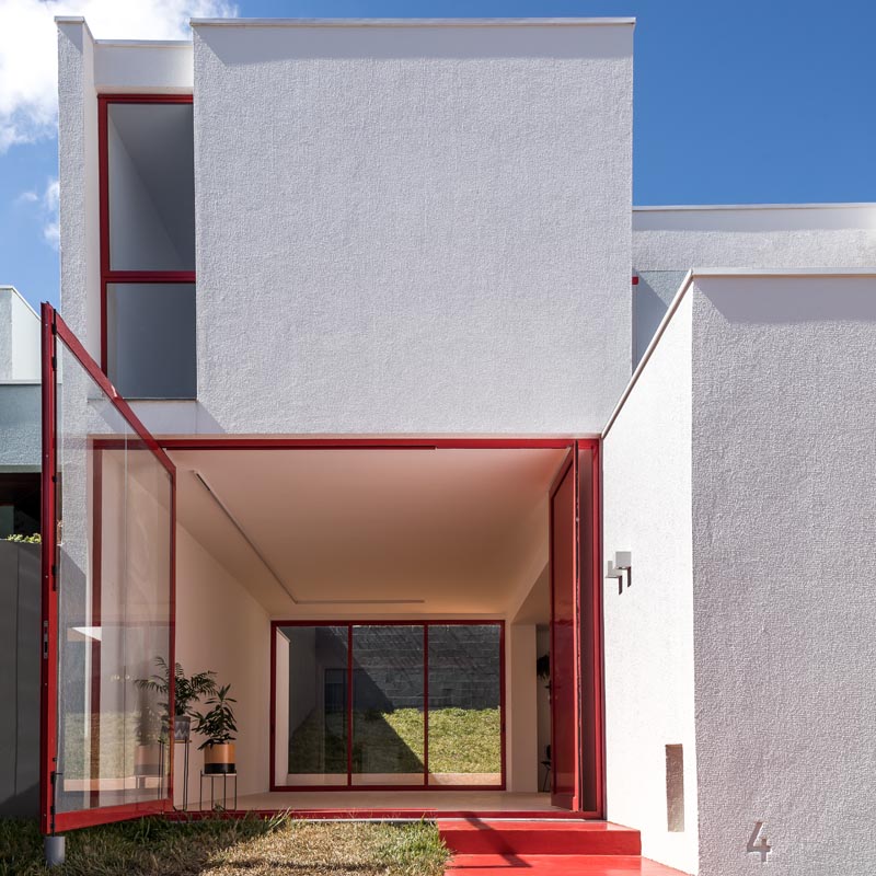 When the front door of this modern house is open, the large pivoting window can be moved by pushing the frame to open it up completely, exposing the interior of the home to the small grass patio. and front yard. #PivotingWindow #RedFrontDoor #WindowIdeas