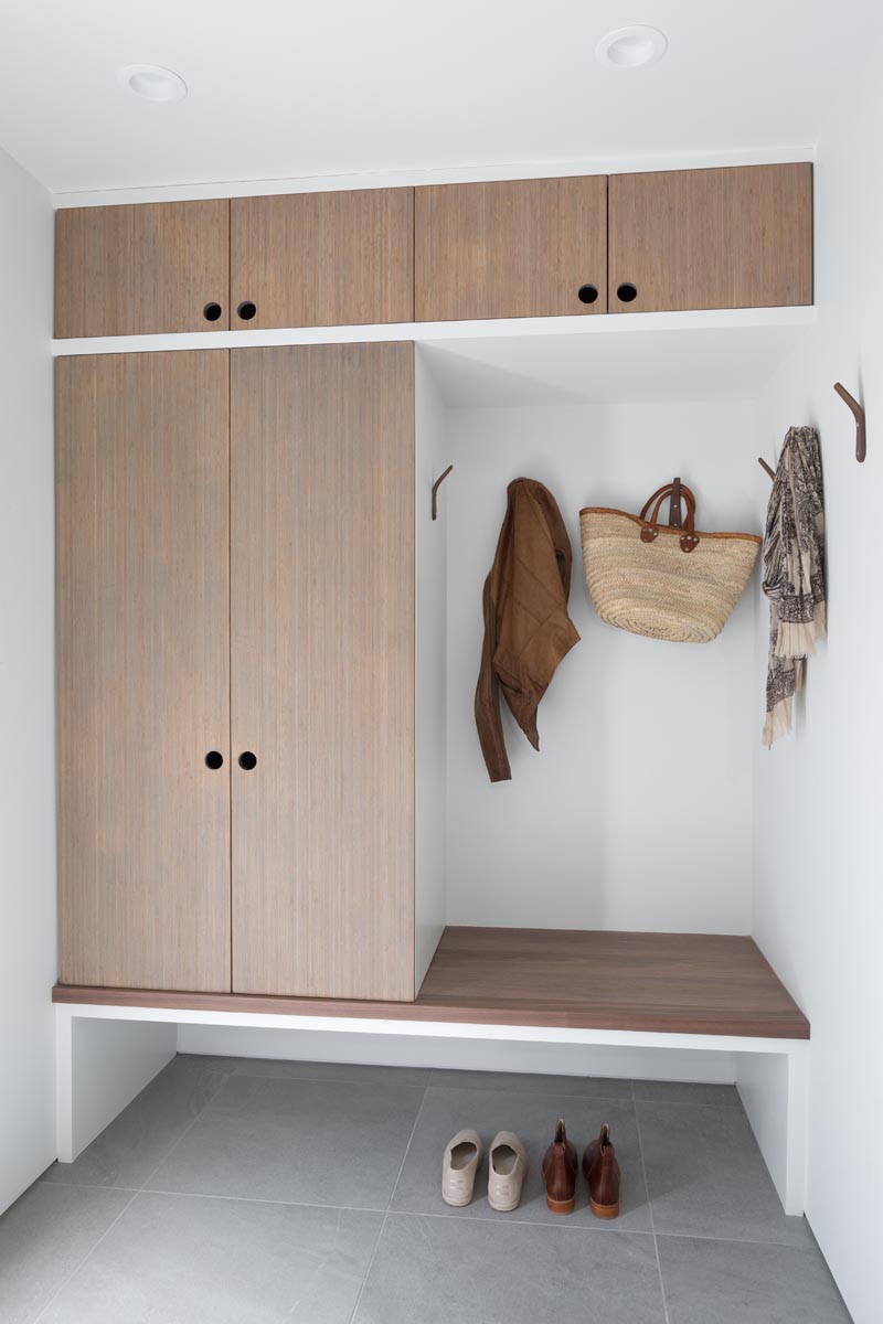 This modern mudroom has custom bamboo cabinetry with a built-in bench. To keep its design minimal, there are finger holes instead of hardware, and wood hooks on the wall. #Mudroom #ModernMudroom #EntrywayIdeas